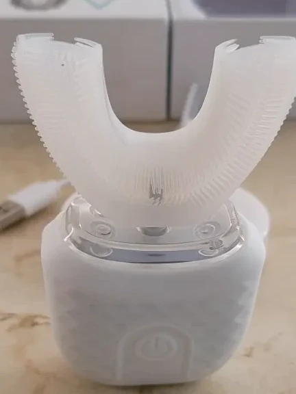 Biała nakładka w kształcie U osadzona na korpusie z jednym przyciskiem, urządzenie stoi na jasnym kamiennym blacie, obok zwinięty biały kabel USB.