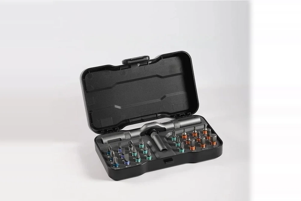 Otwarta walizka Grzechotka: trzonek z głowicą grzechotki, dwa ramiona, magnetyczny uchwyt i komplet bitów z kolorowymi pierścieniami we wkładce z opisanymi gniazdami.