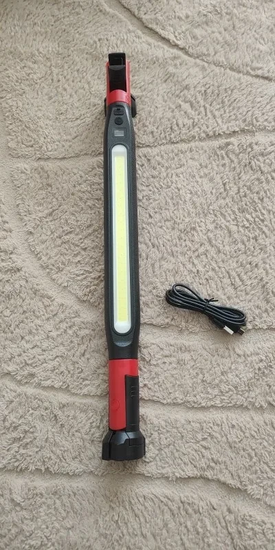 Zdjęcie kupującego: czarno-czerwona lampa z jednym długim oknem światła leży na jasnym dywanie, obok zwinięty kabel USB